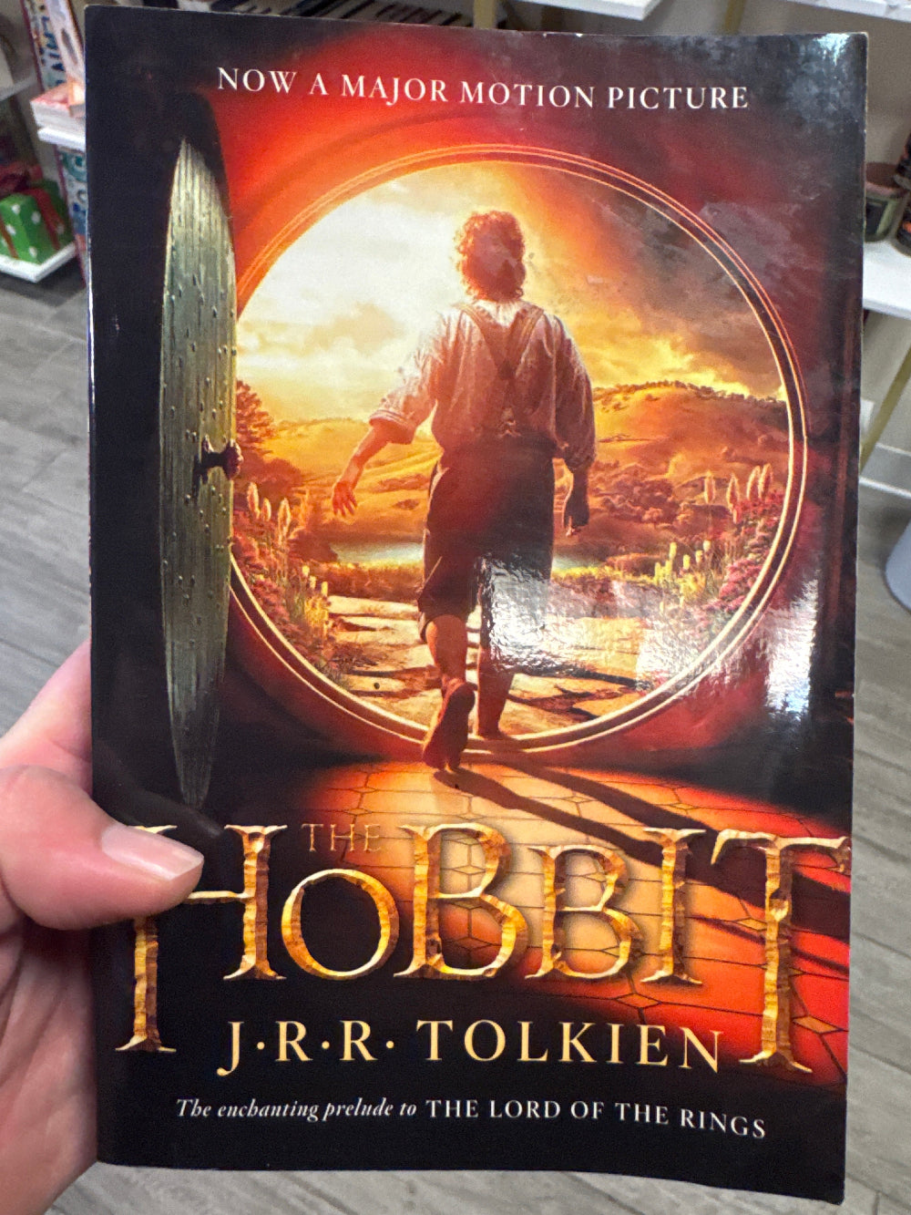 Book titled 'The Hobbit' by J.R.R. Tolkien held in a hand with a motion picture promotion on the cover.