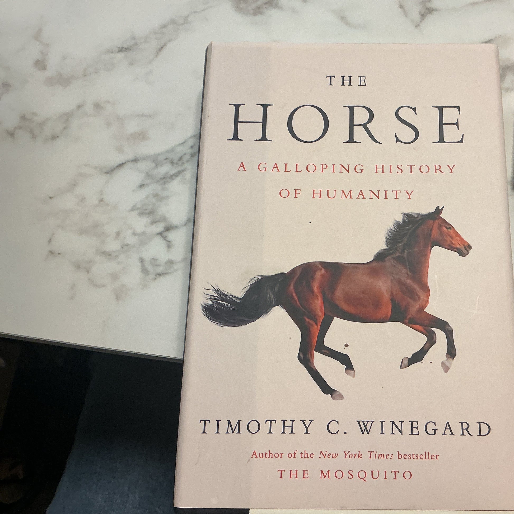 Book titled 'The Horse: A Galloping History of Humanity' by Timothy C. Winegard on a marble surface.