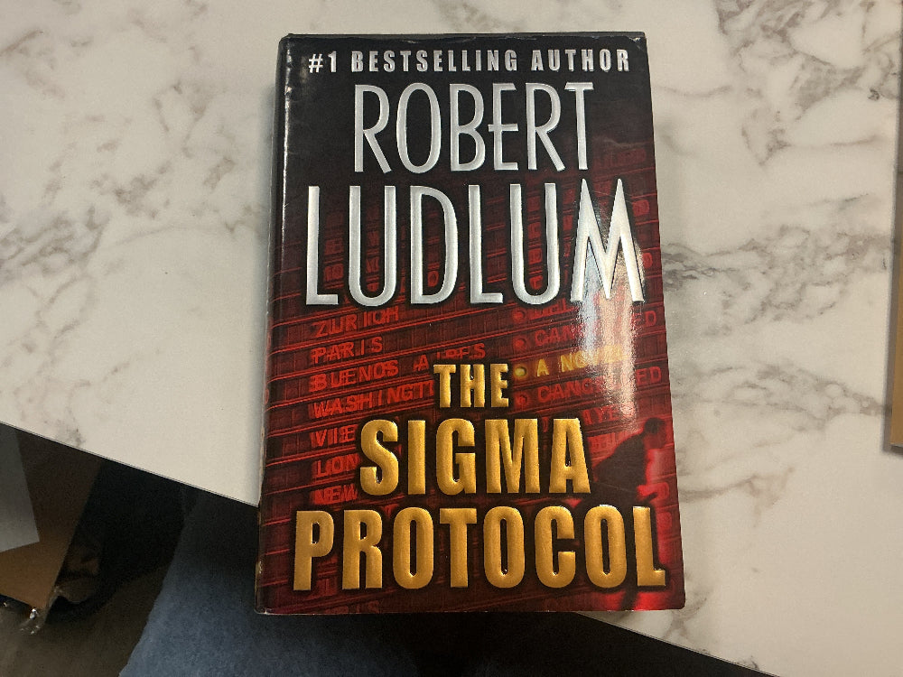 Book titled 'The Sigma Protocol' by Robert Ludlum on a marble surface