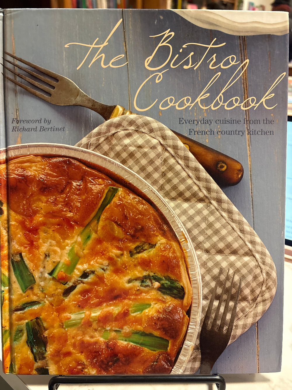 Cookbook titled 'The Bistro Cookbook' with a quiche on top, featuring a fork and oven mitt.