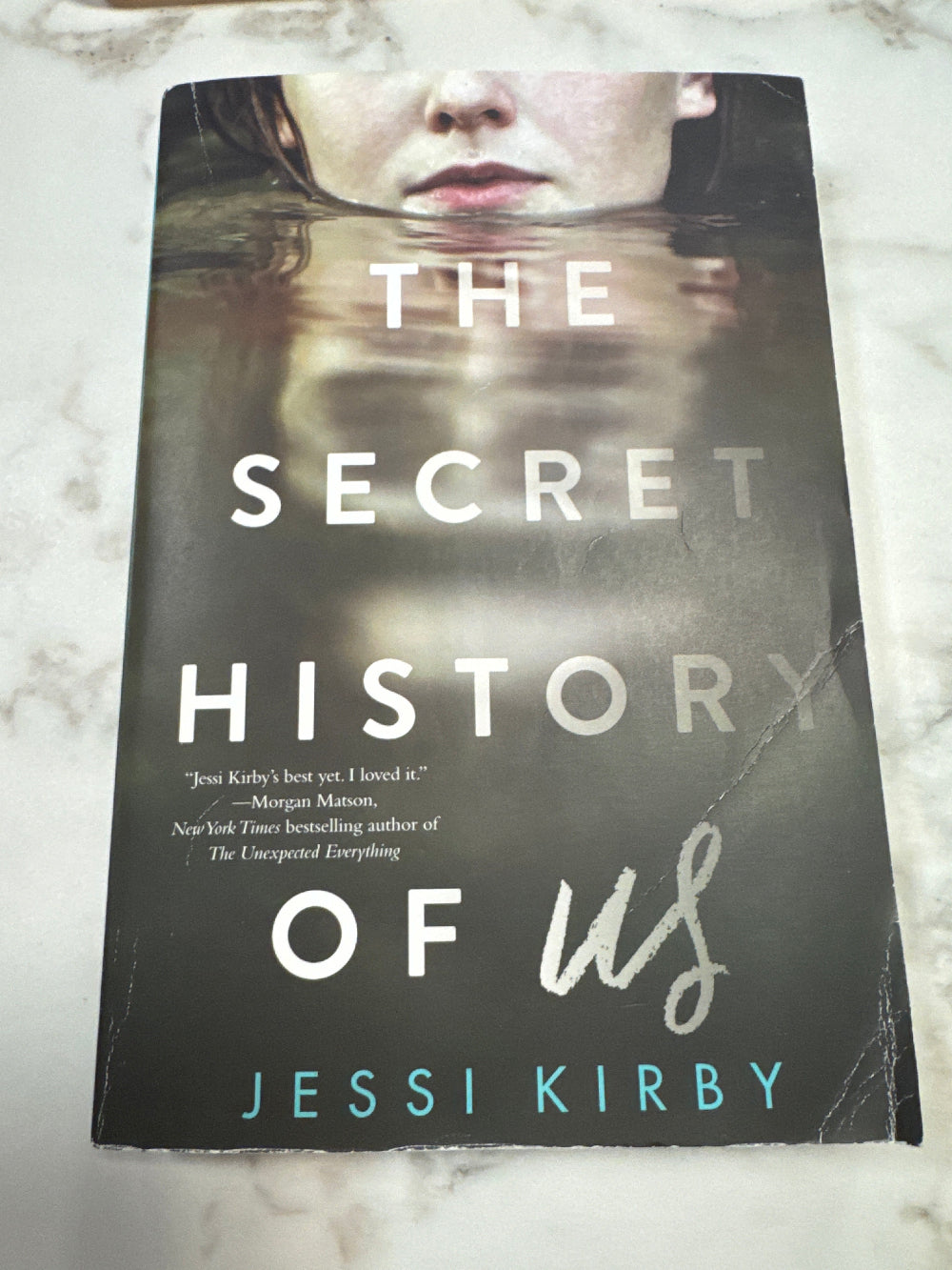 Book titled 'The Secret History of Us' by Jessi Kirby on a marble surface