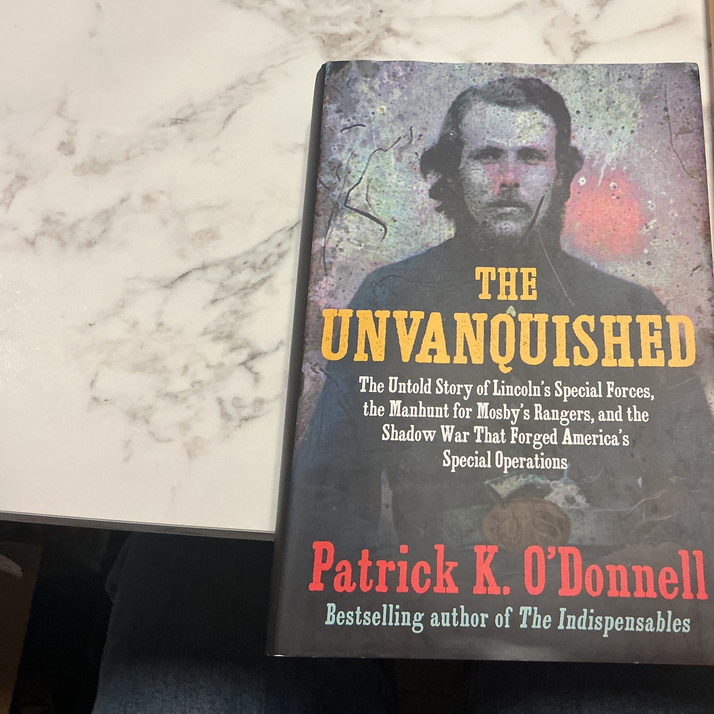 Book titled 'The Unvanquished' by Patrick K. O'Donnell on a marble surface.