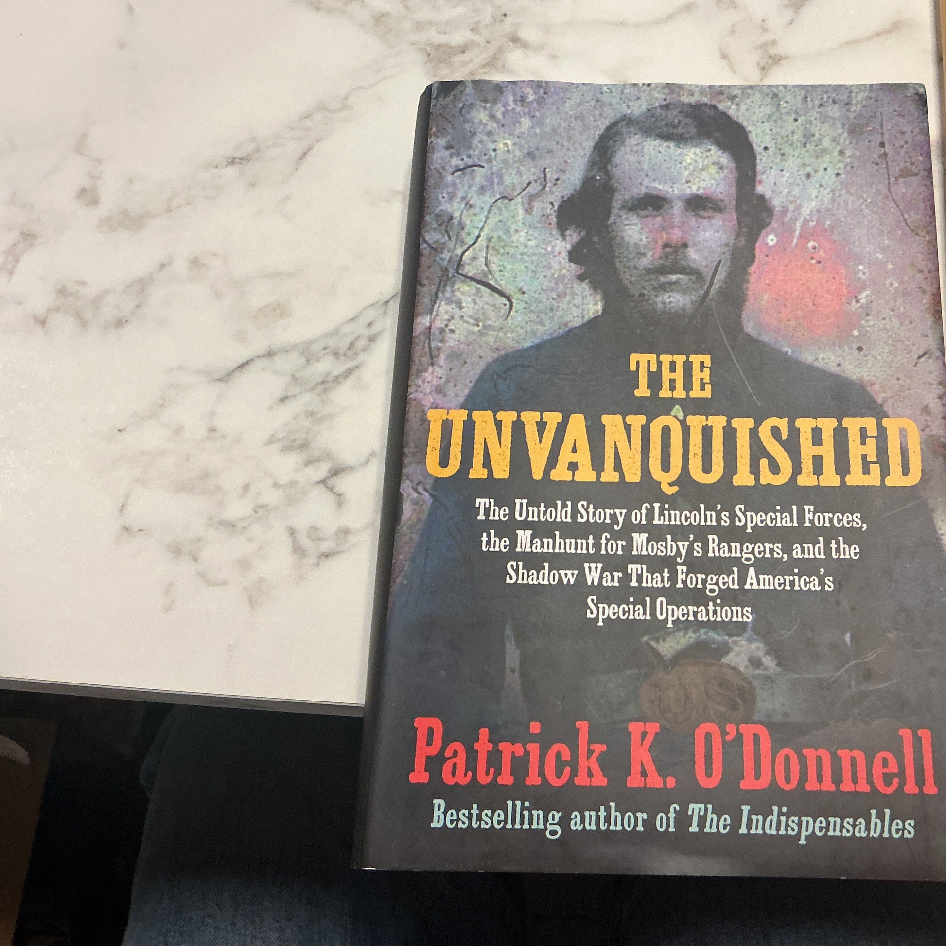 Book titled 'The Unvanquished' by Patrick K. O'Donnell on a marble surface.
