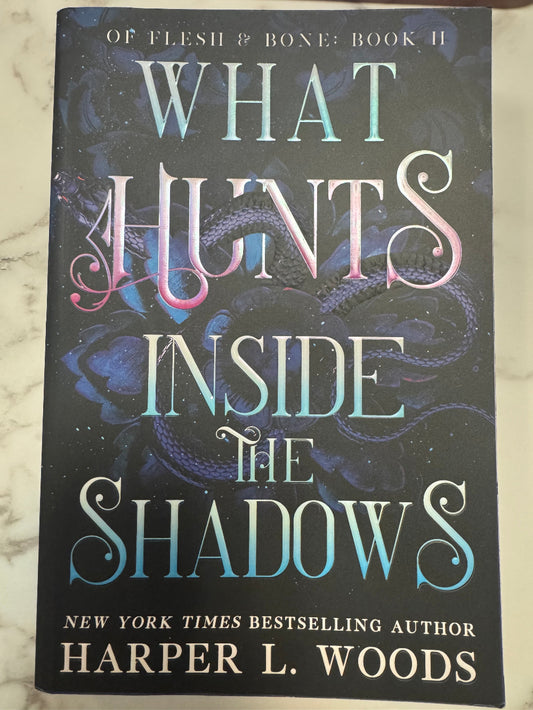 Book cover of 'What Hunts Inside the Shadows' by Harper L. Woods on a marble surface