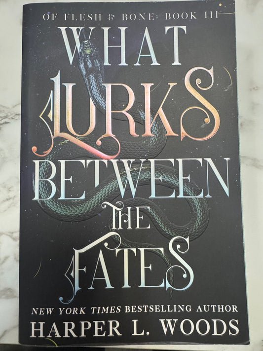 Book titled 'What Lurks Between the Fates' by Harper L. Woods on a marble surface