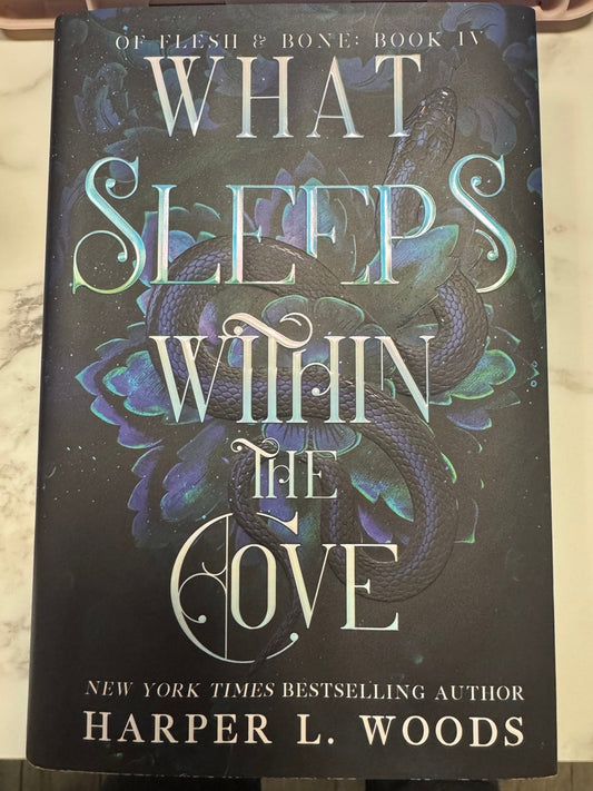 Book titled 'What Sleeps Within the Cove' by Harper L. Woods on a dark background