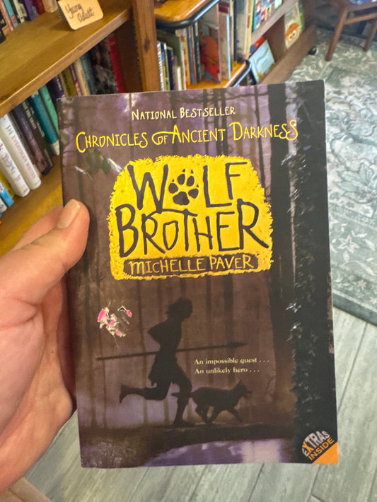 Book titled 'Wolf Brother' by Michelle Paver held in a hand with a blurred bookshelf background